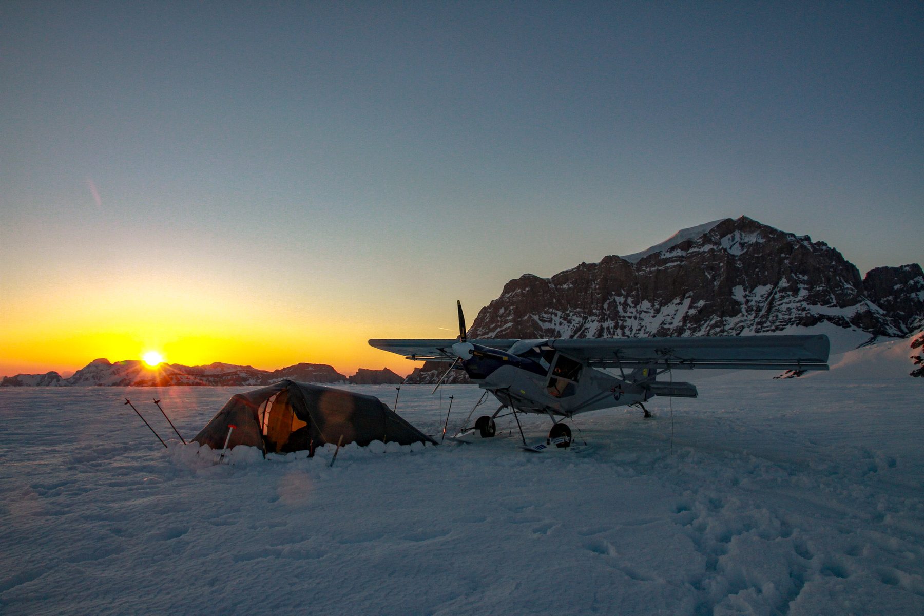 Zelt und Leichtflugzeug im Schnee, die Sonne steht am Horizont