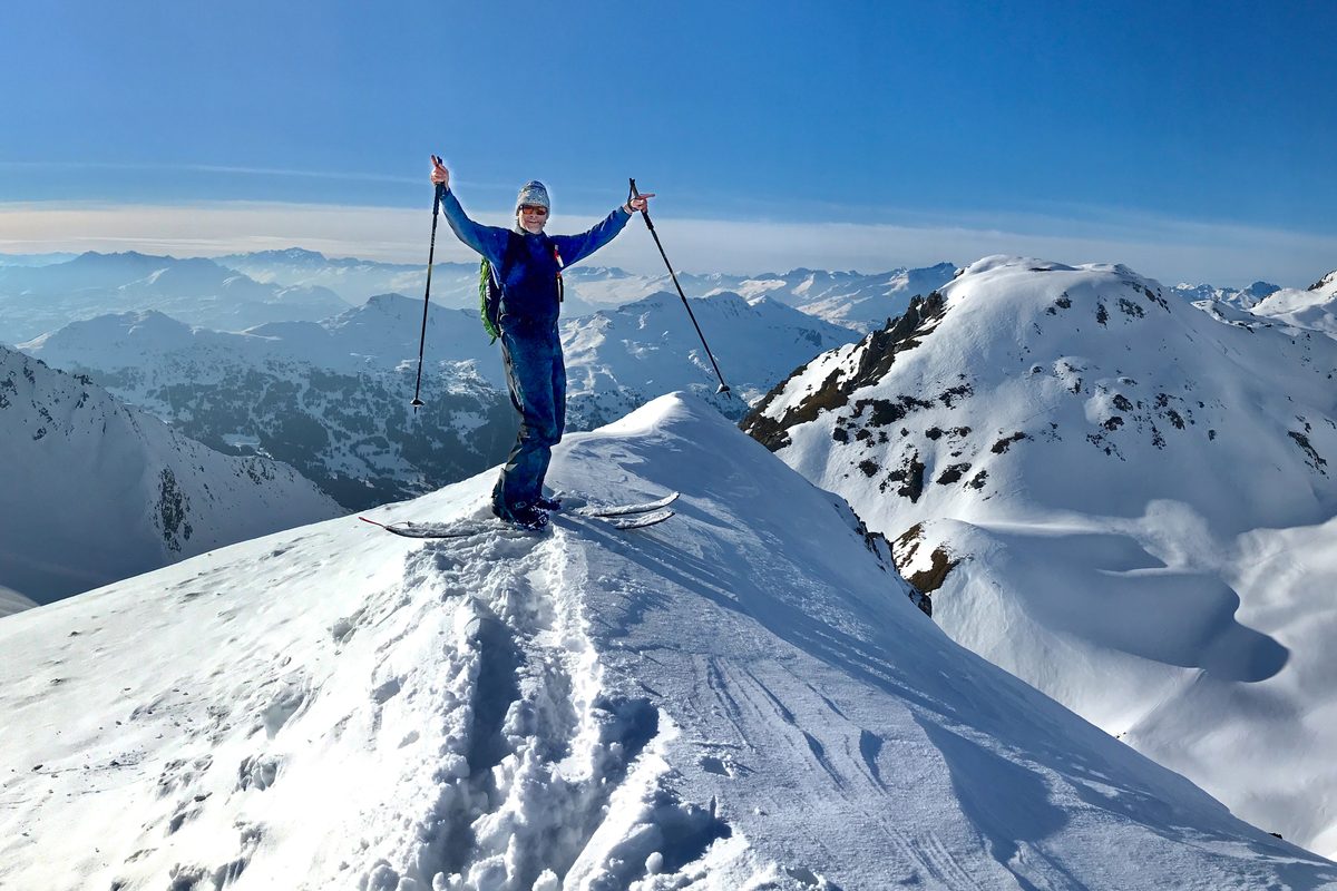 Person mit erhobenen Skistöcken auf einem verschneiten Gipfel
