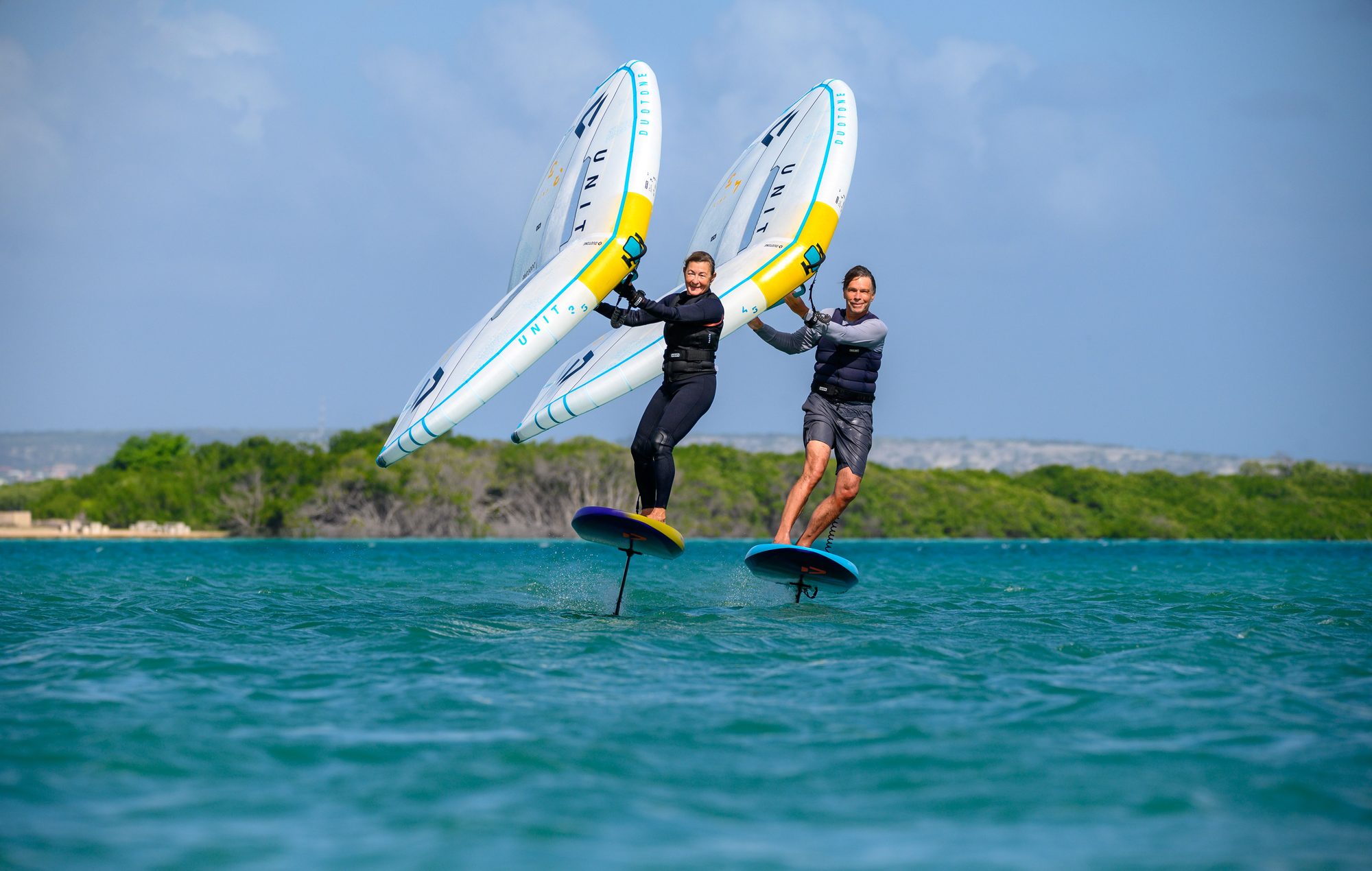 Claudia und Roland nebeneinander beim Wingfoilen auf türkisem Wasser